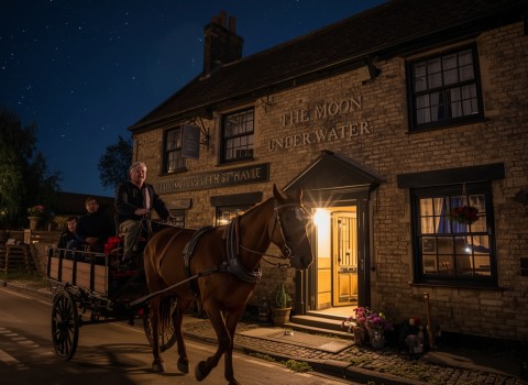 A horse-drawn carriage outside The Moon Under Water at night
